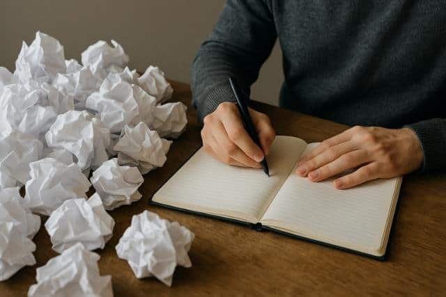 Person journaling to relieve mental overload with scattered crumpled papers.